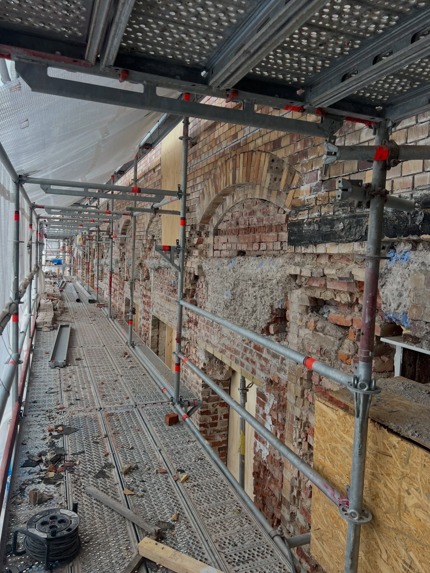 Fasad under renovering där gammalt tegel har rivits fram bakom ställningen