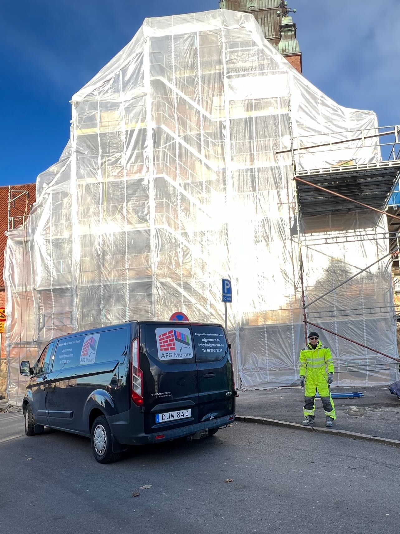 Inklädd ställning runt en byggnad och AFG Murares servicebil på gatan nedanför